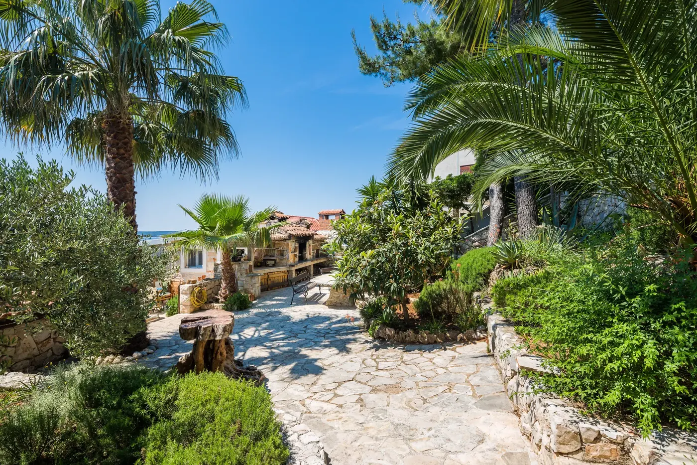 Steinweg durch den mediterranen Garten zum Haus, mit dem Meer im Hintergrund
